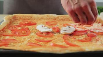 The male chef spreads slices of fresh champignons on a rolled dough, drizzled with tomato sauce and prepares a delicious pizza. video