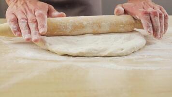 man rolls out dough in the kitchen in close-up. The pastry chef rolls out the yeast dough using a wire rod. video