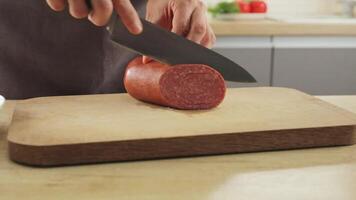 A man cuts salami with a sharp knife in the kitchen. Sausage slicing in close-up. video
