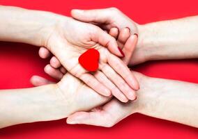 Females and males hands holds red heart on red background. Close-up. Top view. photo