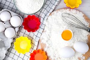 Flour, eggs and colourful silicone form on a table. Ingredients for baking muffins and cupcakes. Top view. photo