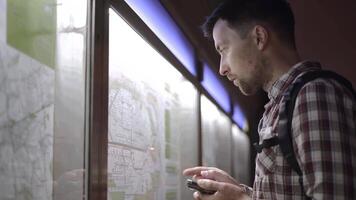 Man is looking at information on backlit board at public transport station in Germany, checking details on his smartphone. Passenger looks at subway train schedule at station on information board. video