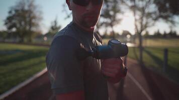 Athlete massages with percussion therapy gun to relieve pain of muscle aches after workout. Man massages his body with massage percussion device after training session. Muscle warming up with massager video
