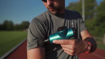 Athlete massages with percussion therapy gun to relieve pain of muscle aches after workout. Man massages his body with massage percussion device after training session. Muscle warming up with massager video