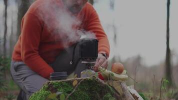 Male hiker uses wok and gas burner to make boiling water while hiking on stump in autumn. Autumn camping. Backpacker enjoys fall by boiling water on a camping stove to make tea and food in the woods. video