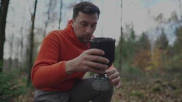 Man hiker sets up system for cooking while camping in woods. Traveler prepares to cook food on burner. Eating and drinking while hiking. Compact and portable cooking systems. Travel gear. Gas stove. video
