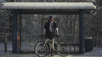 Bicyclist bicycle broke down in winter and he waits long time for bus at snowy stop after snowstorm in Germany. Male cyclist really frozen waiting for transport at standstill for long time in winter. video