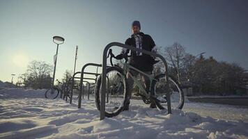 Man cyclist locks bicycle in a street parking lot in Europe in winter snowy weather. Locking bike for parking . Protecting your cycle from burglary. Commuting on a bicycle in the frost. video