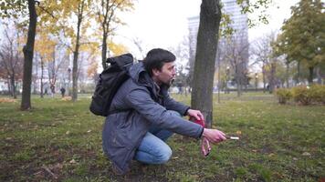 Young Caucasian man looking for a runaway dog in a city park in autumn, holding a bait in his hands and calling for a pet. The theme of people and pets in the city. Finding an obedient husky dog. video