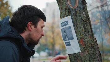 A man reads an advertisement about the loss of a dog in a tree in the park and calls the owner at the phone number indicated in the poster. The theme of the missing search for missing pets. Lost dog video