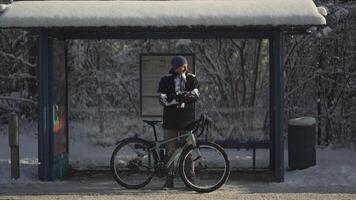 Bicyclist bicycle broke down in winter and he waits long time for bus at snowy stop after snowstorm in Germany. Male cyclist really frozen waiting for transport at standstill for long time in winter. video