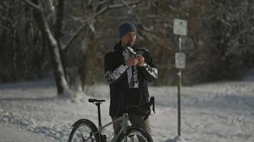 Navigation, GPS positioning, routing, offline map in a smartphone. Male cyclist stopped while cycling in winter in snow to check messages and direction of the journey. Bicycle rides in snowy weather. video