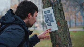 heiser Hund hat Weg fehlt und glücklich Mann hat gefunden es und ist Berufung das Inhaber von ein Werbung auf Baum im Park. das Kerl Zifferblätter das Nummer von das hat verloren Hündchen Poster. Suche zum fehlt Haustiere. video