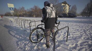 Man cyclist locks bicycle in a street parking lot in Europe in winter snowy weather. Locking bike for parking . Protecting your cycle from burglary. Commuting on a bicycle in the frost. video