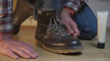 Unrecognizable man cleans brown leather boots with brush and lubricates with cream and blotting protection. Theme shoe care. Boot waxing. Outdoor boots with wax. Accessories for boot caring. video