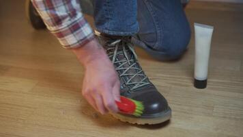 Unrecognizable man cleans brown leather boots with brush and lubricates with cream and blotting protection. Theme shoe care. Boot waxing. Outdoor boots with wax. Accessories for boot caring. video