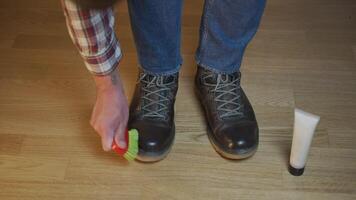 Unrecognizable man cleans brown leather boots with brush and lubricates with cream and blotting protection. Theme shoe care. Boot waxing. Outdoor boots with wax. Accessories for boot caring. video