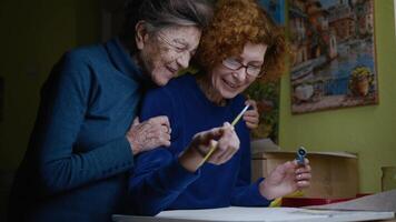 An old mother's visit to nursing home. Drawing lesson with an elderly daughter and senior mother in an art studio. Joint family hobby of two females to paint paintings on canvas. Painting workshop. video