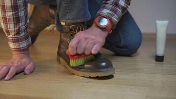Unrecognizable man cleans brown leather boots with brush and lubricates with cream and blotting protection. Theme shoe care. Boot waxing. Outdoor boots with wax. Accessories for boot caring. video