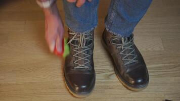 Unrecognizable man cleans brown leather boots with brush and lubricates with cream and blotting protection. Theme shoe care. Boot waxing. Outdoor boots with wax. Accessories for boot caring. video