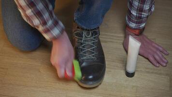 Unrecognizable man cleans brown leather boots with brush and lubricates with cream and blotting protection. Theme shoe care. Boot waxing. Outdoor boots with wax. Accessories for boot caring. video