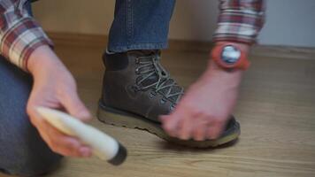Unrecognizable man cleans brown leather boots with brush and lubricates with cream and blotting protection. Theme shoe care. Boot waxing. Outdoor boots with wax. Accessories for boot caring. video