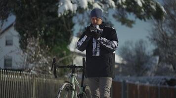 hombre en bicicleta paseo en invierno en congelación Nevado clima detenido y usado un móvil teléfono, utilizando aplicación a encontrar GPS posicionamiento, ruta guía, en línea mapa y navegación mientras andar en bicicleta concepto de viaje. video