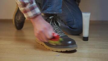Unrecognizable man cleans brown leather boots with brush and lubricates with cream and blotting protection. Theme shoe care. Boot waxing. Outdoor boots with wax. Accessories for boot caring. video
