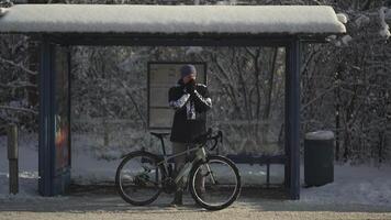 Cyclist extremely cold to ride bicycle in heavy frost and snow in winter and waiting for iced bus at stop, jumping and rubbing his hands. Snowy weather in Germany. A froze commuter on a bus stand. video