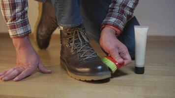 Unrecognizable man cleans brown leather boots with brush and lubricates with cream and blotting protection. Theme shoe care. Boot waxing. Outdoor boots with wax. Accessories for boot caring. video