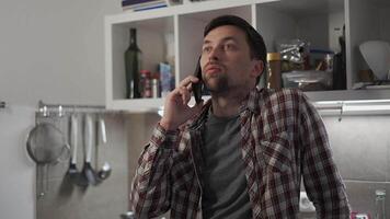 Unhappy male makes phone call requesting some advice in troubled relationship in his kitchen apartment. Sad man discusses private matters by phone with girlfriend in evening at home. Mental problems. video