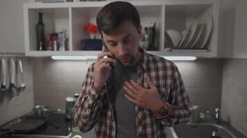 Unhappy male makes phone call requesting some advice in troubled relationship in his kitchen apartment. Sad man discusses private matters by phone with girlfriend in evening at home. Mental problems. video
