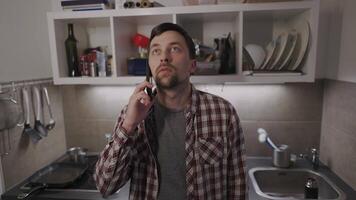 Unhappy male makes phone call requesting some advice in troubled relationship in his kitchen apartment. Sad man discusses private matters by phone with girlfriend in evening at home. Mental problems. video