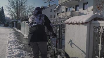 Man cyclist arrived at home on his bicycle in winter in snowy, sunny weather in Germany. Cycling in winter. Male opens gate and enters courtyard of house with bike in freezing temperatures and snow. video