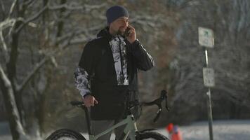Man bicyclist speaking by cell phone from bicycle on cycle trail in snowy, sunny winter weather in Germany. Biking in forest in winter. Staying active and commuting by bike. Environmentally friendly. video