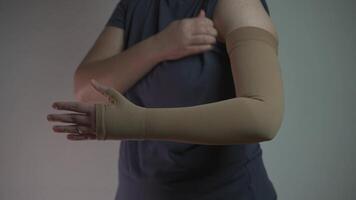 Prophylactics of thrombosis. Woman removes compression sleeve from left hand on gray background. Effective anti-thrombosis therapy involves compression sleeves to improve vein health and blood flow. video