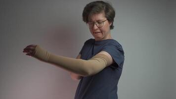 Prophylactics of thrombosis. Woman removes compression sleeve from left hand on gray background. Effective anti-thrombosis therapy involves compression sleeves to improve vein health and blood flow. video