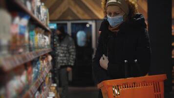A shopper in supermarket puts groceries in basket, wears medical gloves and face mask to avoid contracting the coronavirus during an epidemic. Safe shopping and personal protective equipment theme. video