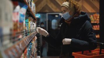 Senior caucasian woman reads the composition of food so as not to cause food allergies, uses a medical mask and protective gloves. The topic of organic and healthy eating, protection from disease. video