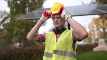 Engineer at green energy company, wearing yellow helmet on head and getting ready for work day. Project supervisor of sunny energy project in protective gear wearing helmet in front of solar panels. video
