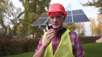 Power engineer standing at solar photovoltaic array and on radio. Construction engineers use a walkie-talkie to communicate with technicians in solar power plants. solar power generating station. video