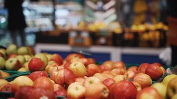 Red apples on shelf in supermarket. Grocery store, fruit section. Focus on apples on blurred background customer walks with basket and chooses product. Shopping theme during COVID 19 coronavirus. video
