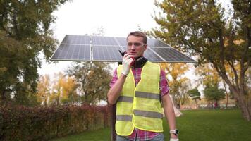Head of sun project, wearing hard hat in front of solar panels and walks talking to his subordinates over walkie talkies. Solar substation engineer wears a yellow helmet and speaks over the radio. video