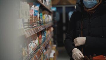 Attentive middle aged caucasian woman inspects groceries before putting them in a shopping cart in a supermarket with no people around, aintains social distance to counteract respiratory disease. video