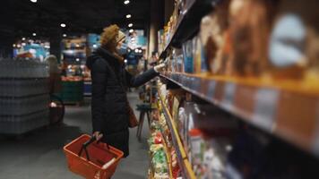 Senior caucasian woman reads the composition of food so as not to cause food allergies, uses a medical mask and protective gloves. The topic of organic and healthy eating, protection from disease. video