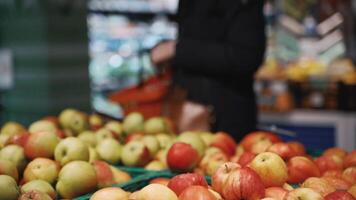 Red apples on shelf in supermarket. Grocery store, fruit section. Focus on apples on blurred background customer walks with basket and chooses product. Shopping theme during COVID 19 coronavirus. video