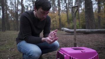 Theme is death and difficult farewell to best friend pet. Male sits next to body of cat in carrier for animals before funeral and mentally asks for forgiveness while holding animal food in his hands. video