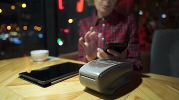 Female mature customer holding phone near nfc terminal make contactless mobile payment on coffeeshop counter, senior woman client pay in cafe with cellphone via pos machine. POS terminal. video