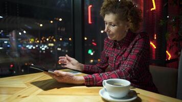 Senior woman using tablet in a cafe. Mature woman relaxing at a restaurant with tablet pc. Elderly female use digital tablet at coffee shop. Technology, old age and people concept. Mature student. video