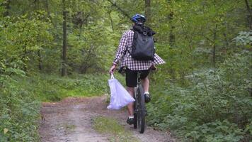 Athlete cycling riding through forest with garbage bag on the handlebars, cleaning up garbage and plastic during a bicycle trip in the forest. Ecology theme, pollution, rubbish and plastic discarded. video